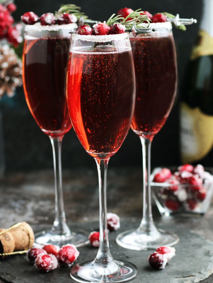 These Cranberry Mimosas with orange liqueur, champagne and cranberry juice are perfect for holiday entertaining. A sugared rim with rosemary and sugared cranberries makes this cocktail colorful and festive.