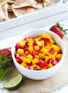 This Strawberry Mango Salsa with Cinnamon Tortilla Chips is simple to make and the perfect, refreshing summertime appetizer.  Fresh strawberries and mangoes get added to this flavorful salsa with a touch of lime juice and mint.  Tortillas get brushed with melted butter, sprinkled with cinnamon and sugar, and cut into triangles before baking into a crispy chip.