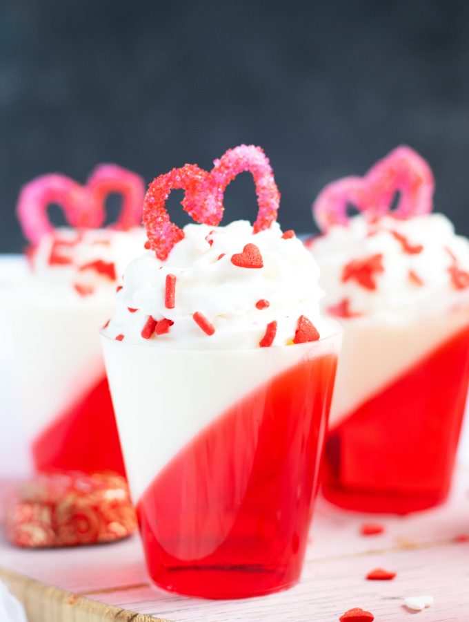 These Strawberries and Cream Layered Jell-O Shots are a festive Valentine's Day treat with whipped cream vodka.  A heart made out of melted white chocolate and sugar sprinkles makes the perfect topper.
